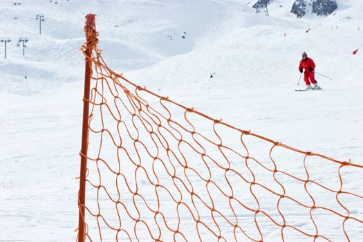 Red fence at ski slope with moving skier at background