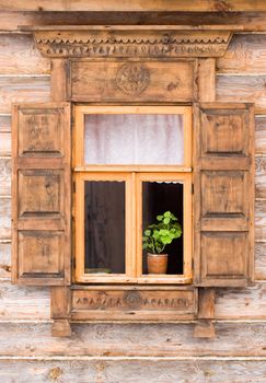 Flower in a pot behind the traditional russian decorated window