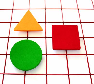 a green circle, a red square and a yellow-orange triangle on a red grid on white