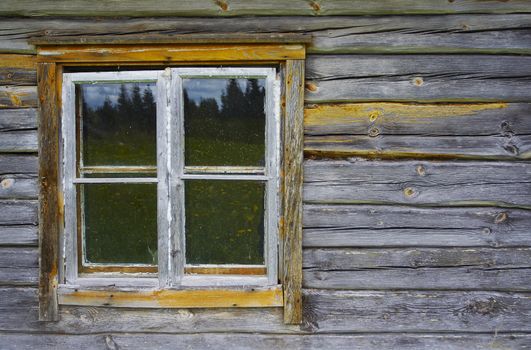 Ancient wood cabin window reflecting summer landscape