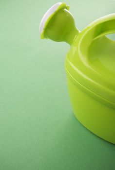 Green toy watering can on green background