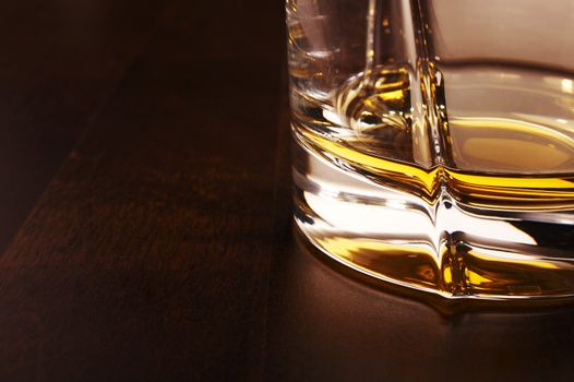 Part of the whiskey glass over a dark wooden table