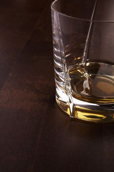 Part of the whiskey glass over a dark wooden table