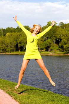 The happy girl jumps on the bank of the summer river