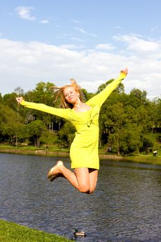 The happy girl jumps on the bank of the summer river