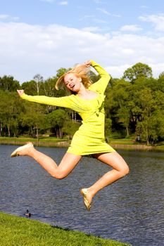 The happy girl jumps on the bank of the summer river