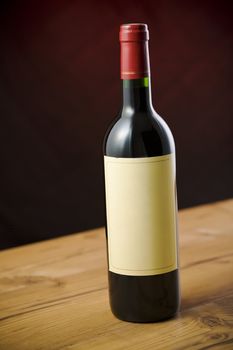 Red wine bottle on wooden table over dark red background