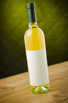 White wine bottle on wooden table over dark green / yellow background