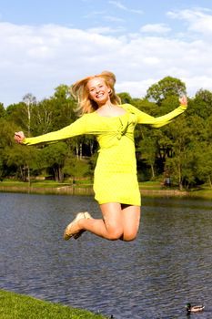 The happy girl jumps on the bank of the summer river