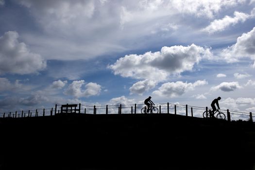 two friends riding moutain bikes - silhouettes agains blue sky