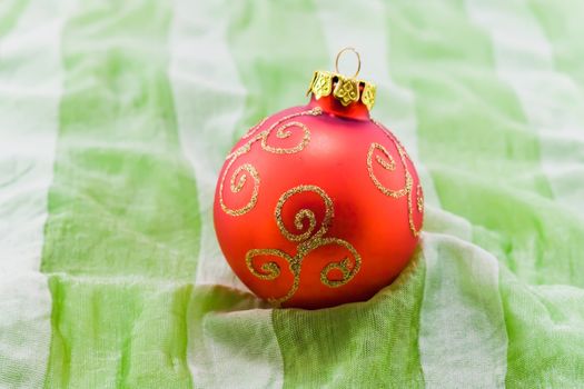 Red christmas-tree ball on green textile with grey stripes