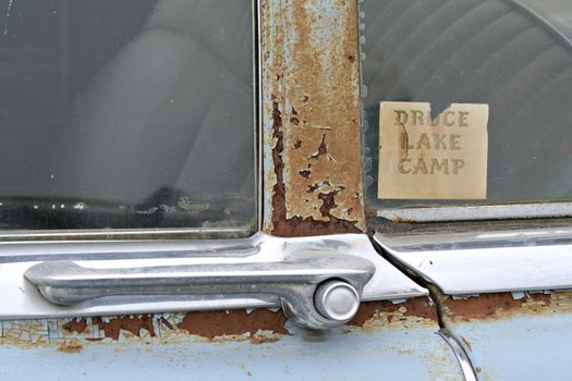 A closeup of an old abandoned car window with a vacation camp ground sticker