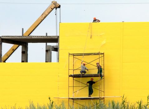Workers on scaffolding on yellow wall background