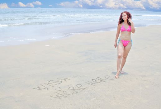 Postcard image of woman writing wish you were here in the sand