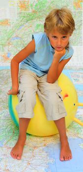 Blond Boy Sitting On The Ball Near The Map