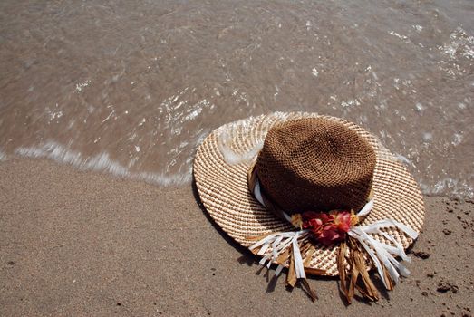 Straw hat laying on the beach is washed by sea surf