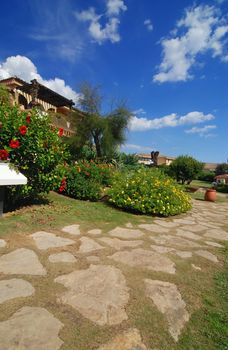 House/hotel in the beautiful summer garden with hibiscus and path - blue sky with clouds above