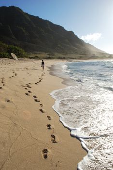 Footprints in the sand leading to a girl walking along a beach on the northern shore of Oahu (beach often used in the filming of television show "Lost")