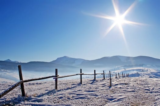 Wooden fence in snowcovered mountains under shiny sun