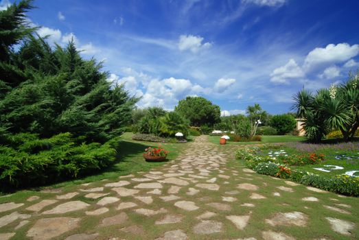 Beautiful park garden with a stone path, many flowers and a blue sky 