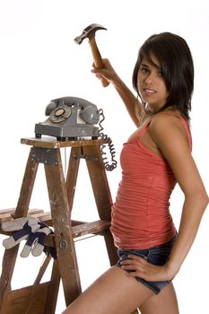 teenage girl standing on ladder about to smash old rotary phone with a hammer
