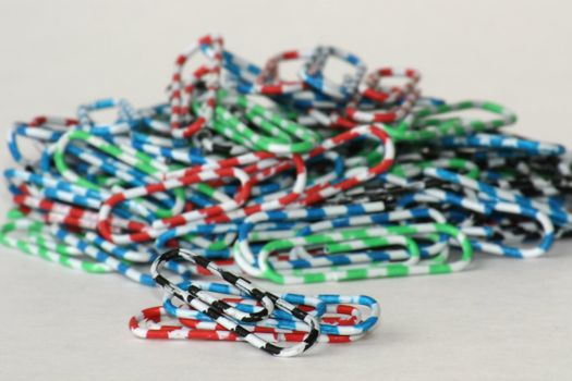 Close view of multicolored paper clips amassed in a pile on a white background. Close-up of brightly colored paper clips in pink red blue white yellow green sit in a pile over white.
