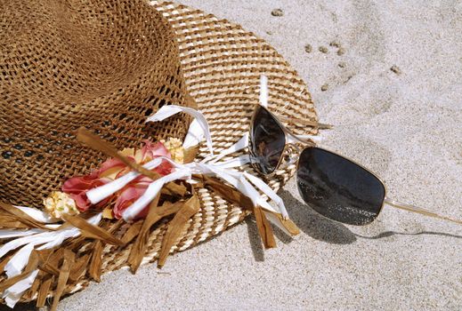 Hat and sun glasses are laying on the beach in the white sand