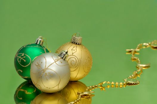 Green and golden baubles and garland on glossy paper