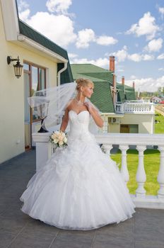 Beautiful blonde bride with bunch of roses on the balcony