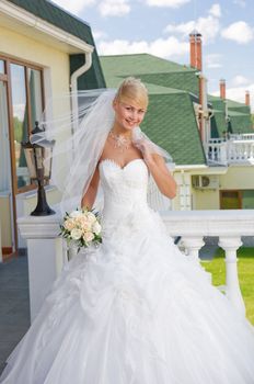 Beautiful blonde bride with bunch of roses on the balcony