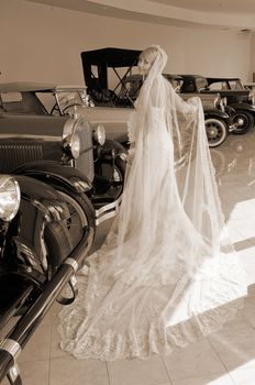 Retro styled picture with beautiful bride standing next old cars.