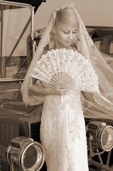 Retro styled picture with beautiful bride standing next old car.