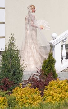 Beautiful blonde bride with fan in the garden at the wall