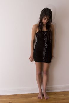 Teenager girl in little black dress standing barefoot against a wall