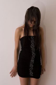 Teenager girl in little black dress against a wall holding her head down