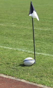Rugby ball near a flag on the field.There are some intended glare areas on the ball.