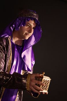 Wise man in the warm light of evening, arrayed in purple and gold thread, holding a golden box filled with frankincense, also known as olibanum.  