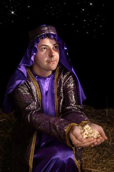 Wise man arrayed in majestic purple robe woven with gold metallic thread is offering in his palms finest pure frankincense. Focus to face.