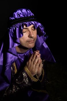 Man arrayed in purple and gold robe with hands together praying