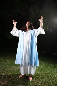 Man wearing white robe and over cloak standing outdoors bathed in light praising and glorifying God.   From (Psalm. 29:2) Give unto the Lord the glory due unto his name; worship the Lord in the beauty of holiness