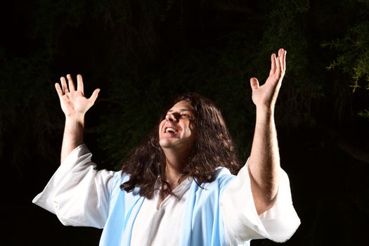 A man dressed in robe hands raised in the air praising or worshipping God on a dark background.