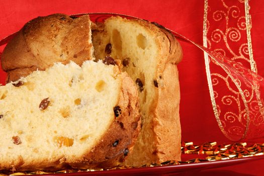 Panettone the italian Christmas fruit cake served on a red glass plate over a red background with red and golden ribbon. Selective focus.