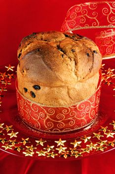 A freshly baked Panettone, the italian Christmas fruit cake with red and golden ribbon served on a red glass plate over a red background.