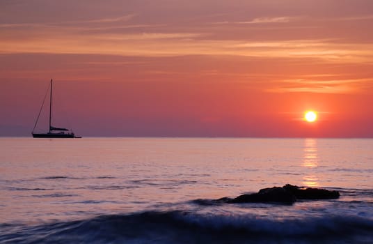 Sailing boat silhouette and rock with surf at sunrise