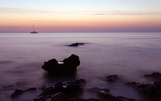Sailing boat silhouette and rocks at  sunrise
