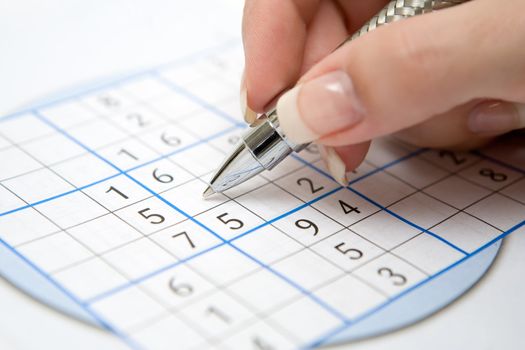Female hand holding pen and doing a Sudoku game.