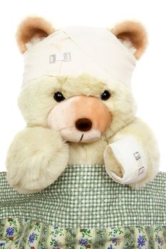 Bandaged teddy lying in bed. Isolated on a white background.
