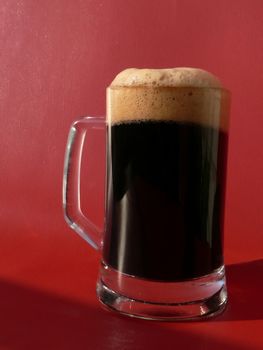 Mug of dark beer on red background