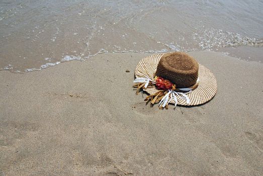 Straw hat laying on the beach is washed by sea surf