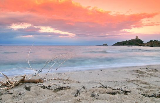 Fairytale sunrise on Sardinia - beach is washed by surf, lighthouse in the back